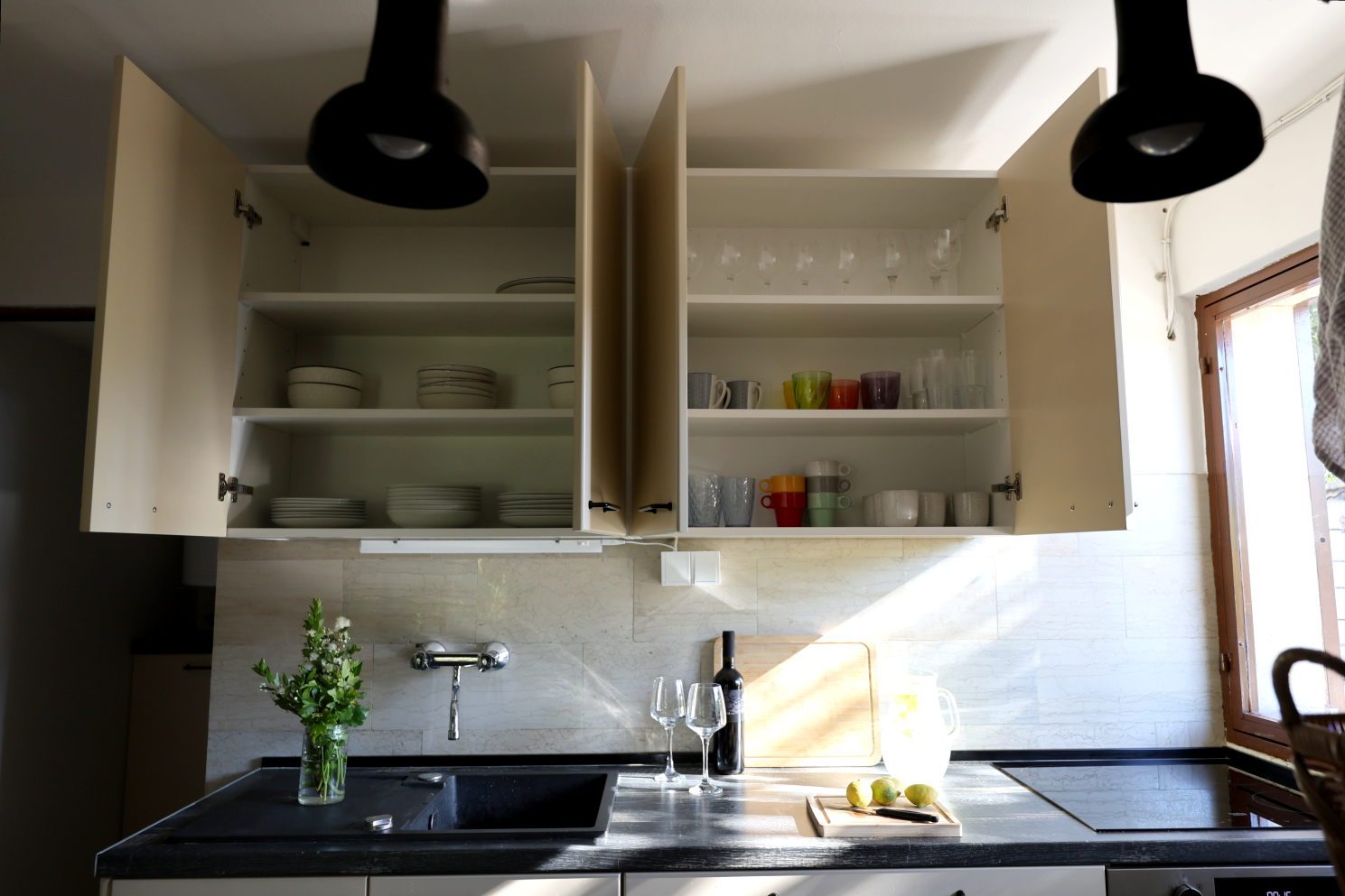 Open kitchen cupboards with plates and glasses, afternoon light across the counter