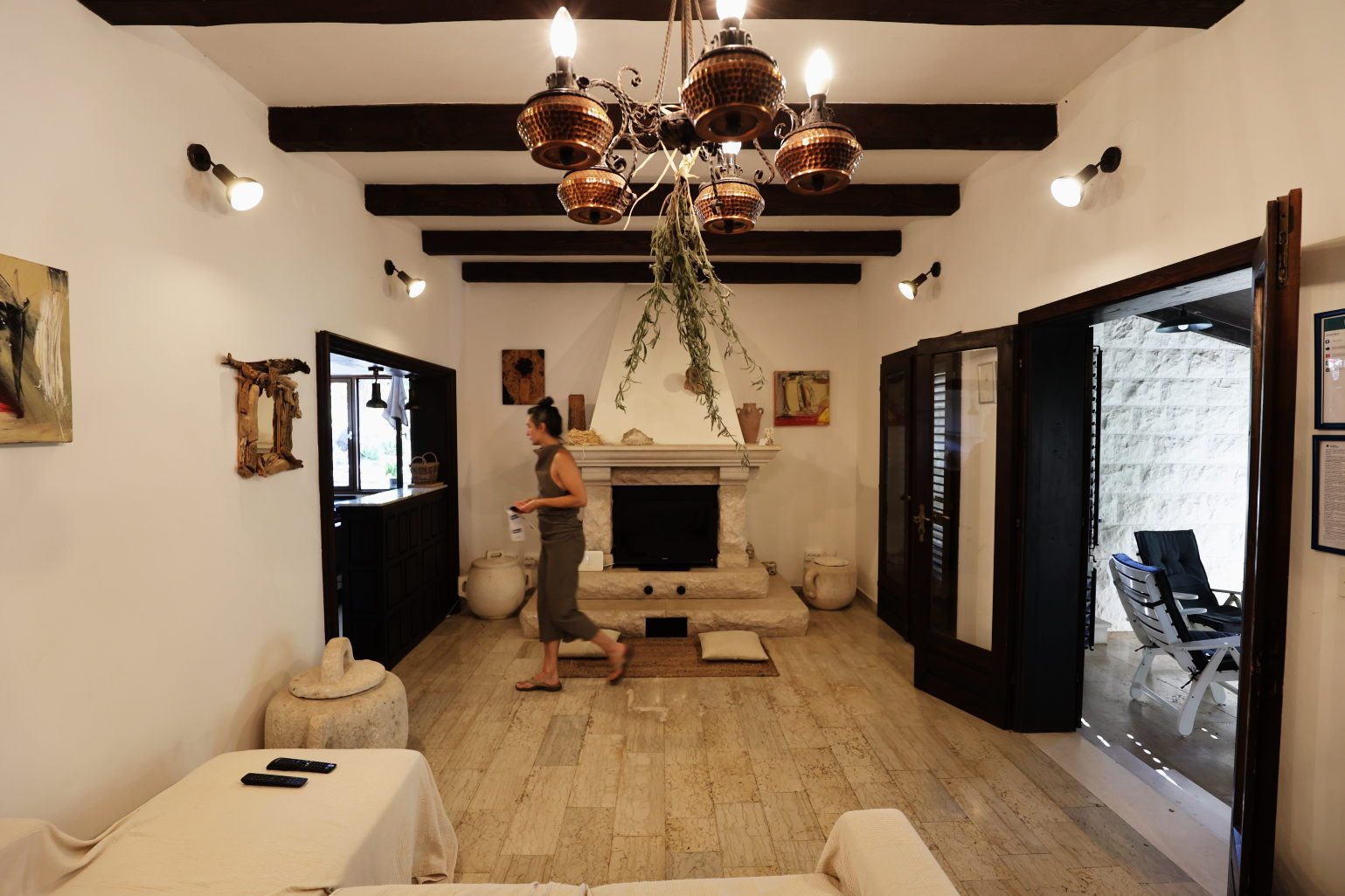 The living room with its stone fireplace under dark timber beams, someone passing through