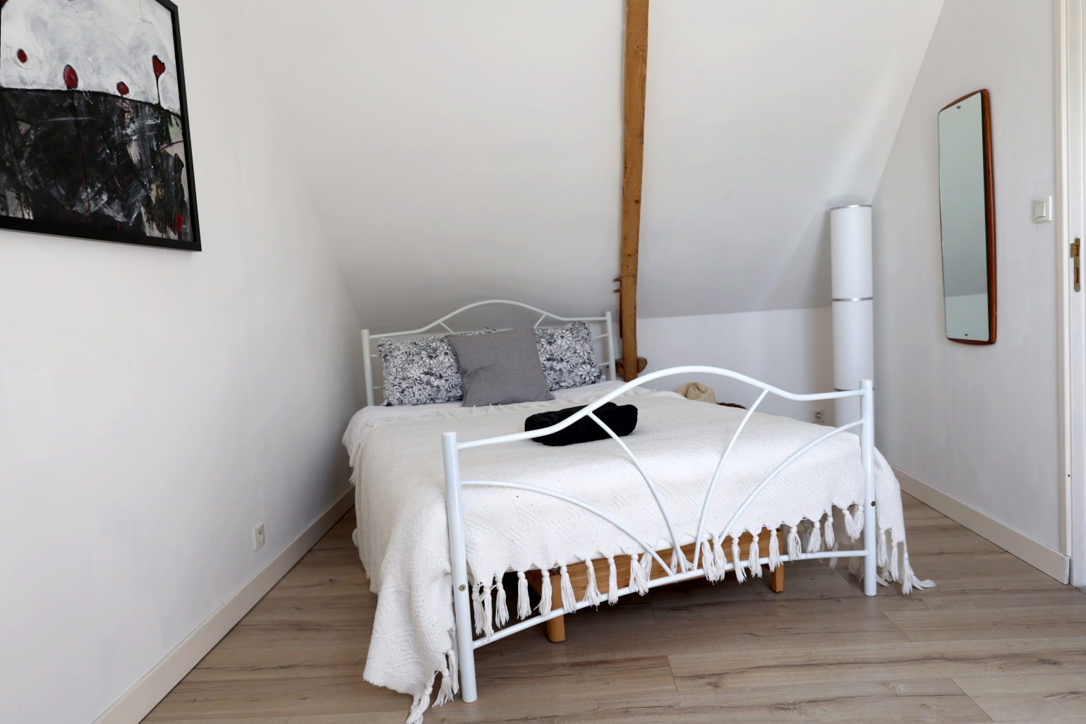 Attic bedroom with a white iron bed, an exposed timber post and a large painting