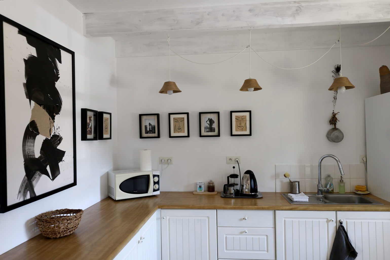 The kitchen counter beneath woven pendant lamps and small framed drawings