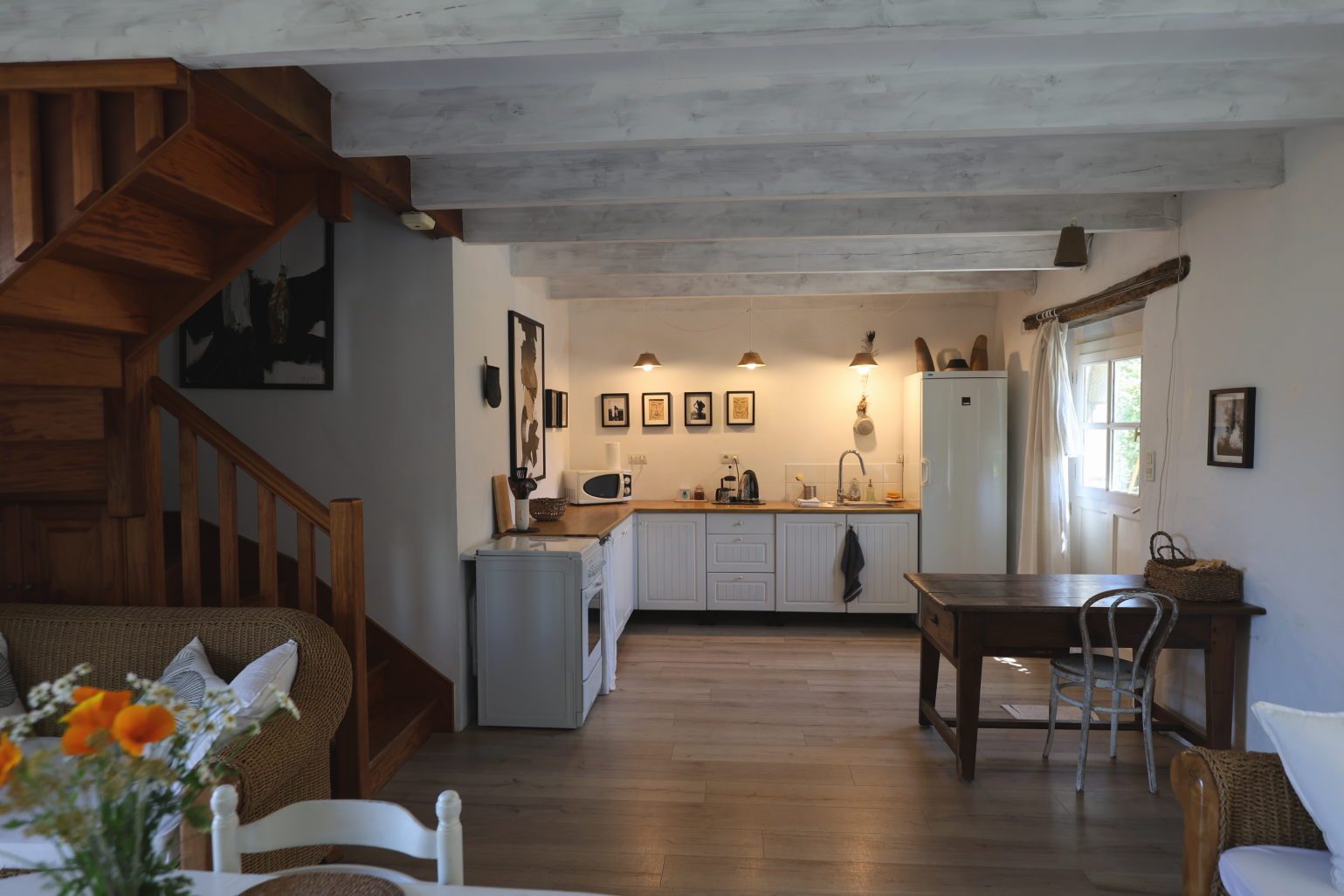 The open kitchen beneath whitewashed beams, with the wooden staircase and an old farmhouse table