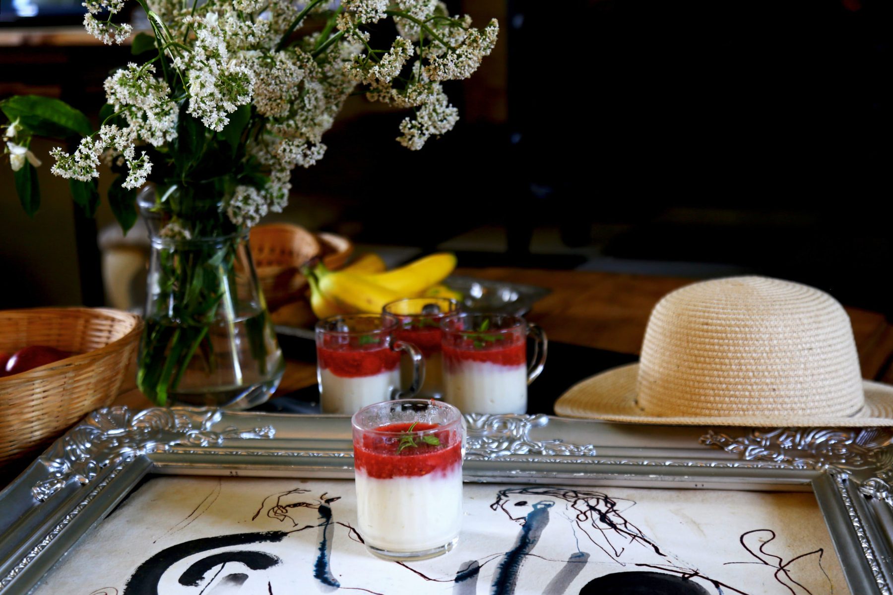 Desserts, garden flowers, a straw hat and artwork on the table