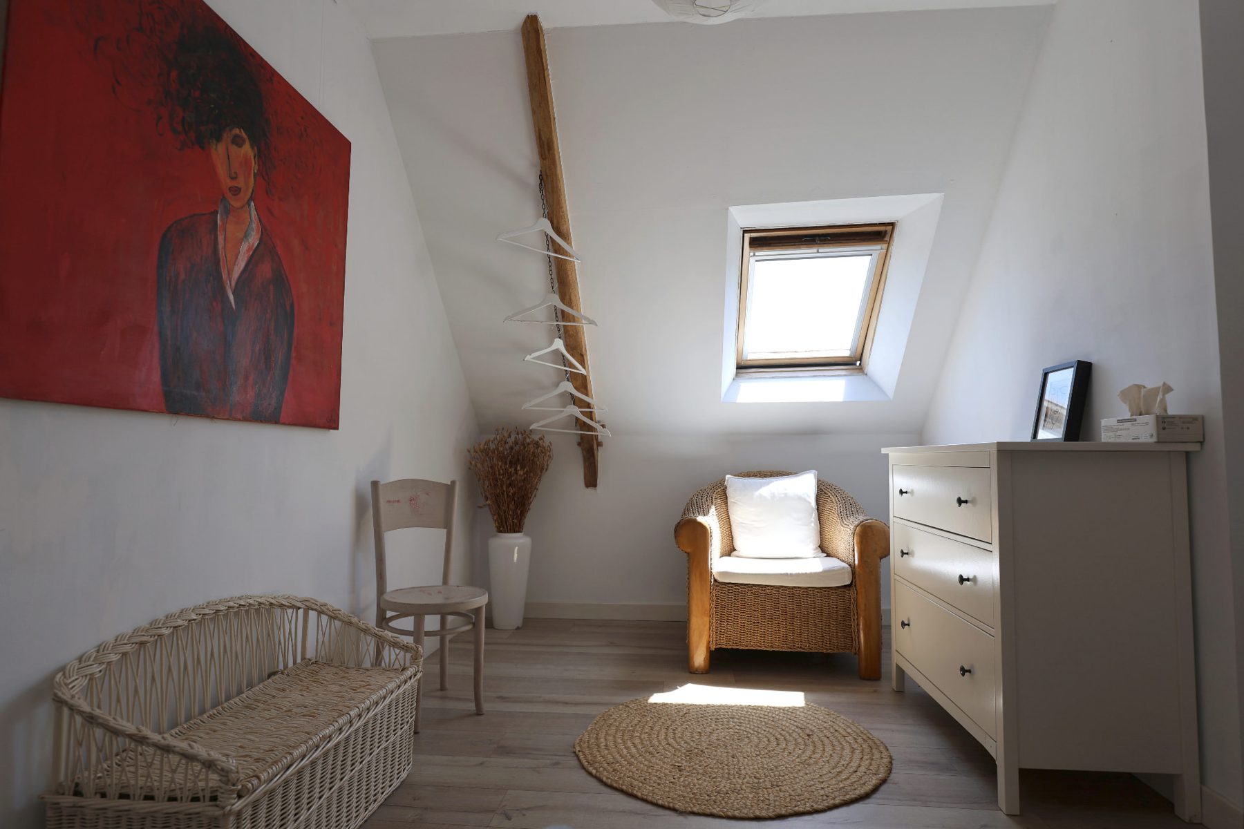 Upstairs sitting space with a red painting, wicker bench and skylight